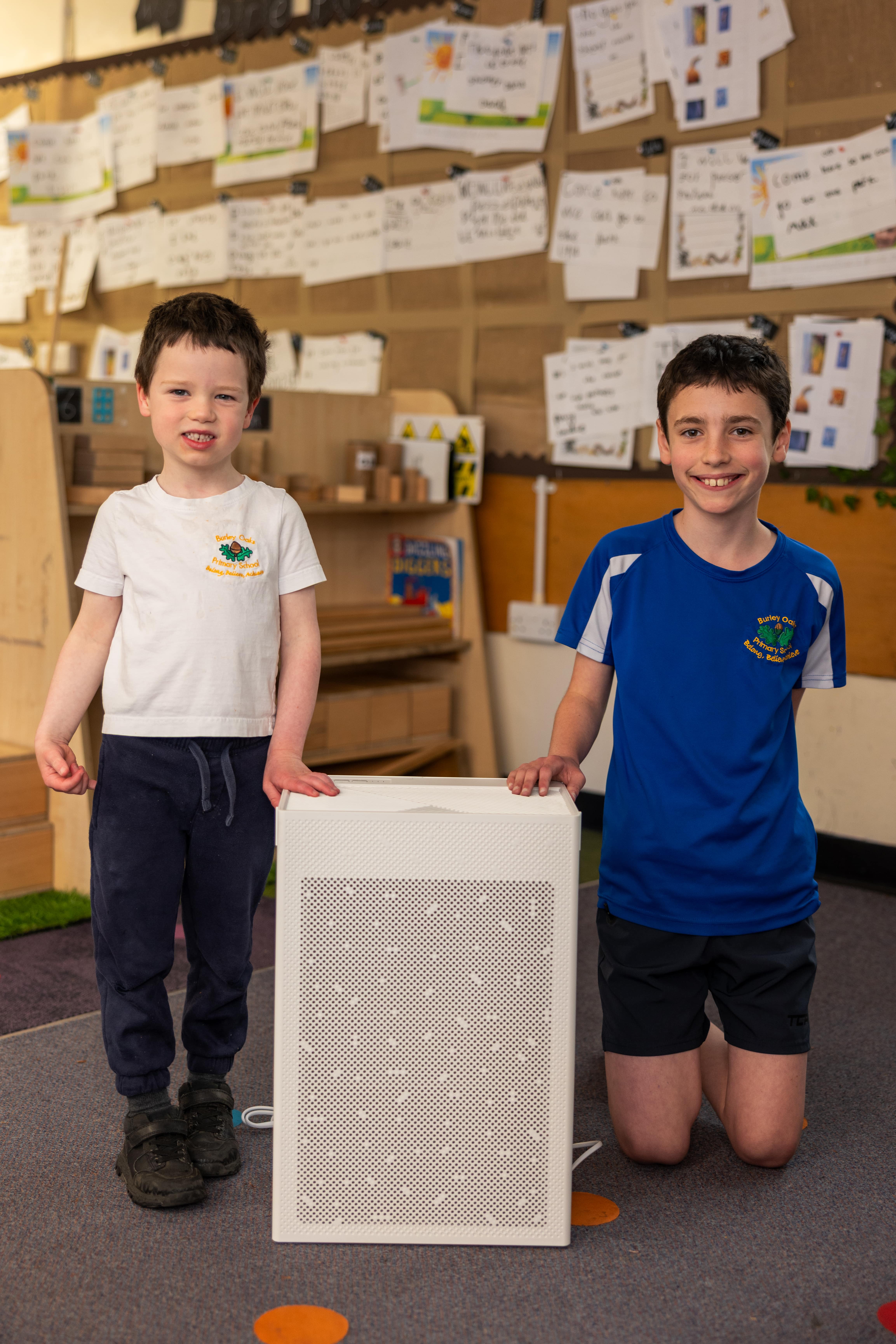 Two pupils at Burley Oaks Primary School standing beside an air cleaner in their classroom